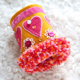 Produktbild: Handsytt armband i gult tyg med rosa hjärtan och paljetter på.