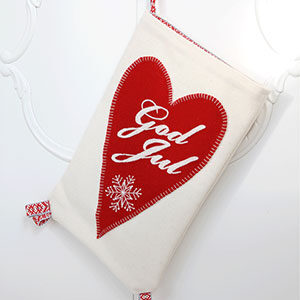 Produktbild: En vit handsydd Julkortsficka med ett hjärta på. På hjärtat är God Jul broderat och även en vit snöflinga